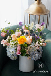 Colorful flower arrangement in a white vase on a teal couch with a gold lantern in the background.