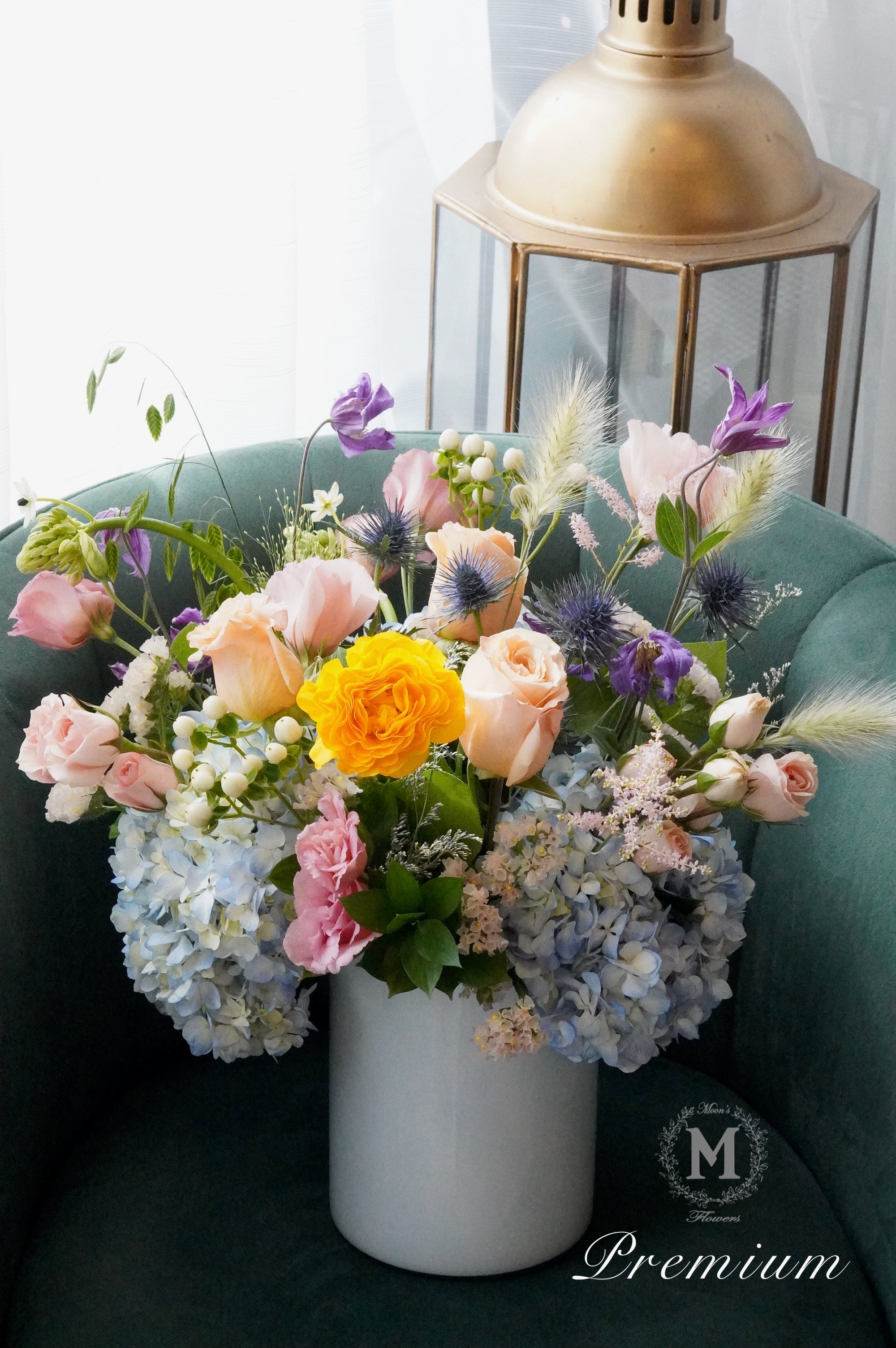 Colorful flower arrangement in a white vase on a teal couch with a gold lantern in the background.
