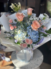 A bouquet of flowers including Hydrangeas, Roses, Statice, Agapanthus, and Thistles with a dreamy color palette of blues, pinks, and champagnes.