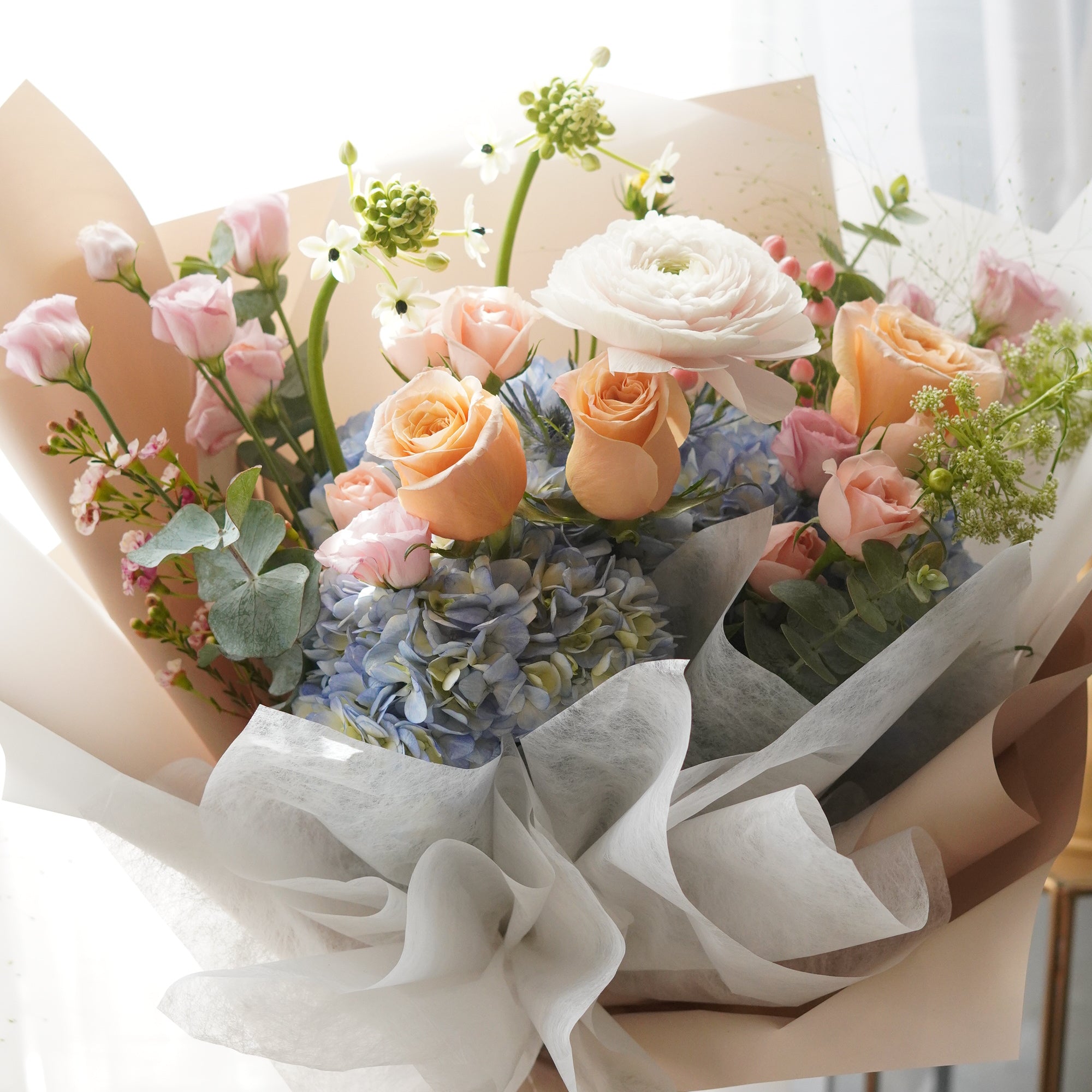 Golden Hour Mother's Day bouquet featuring a premium mix of peach roses, soft blue hydrangeas, and white ranunculus. Elegant hand-tied floral gift by Moon's Flowers Toronto, perfect for same-day delivery