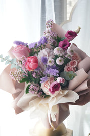 Hand-tied Mother's Day flower bouquet featuring blush pink peonies, purple roses, and lavender stock, wrapped in premium soft-toned paper for delivery in Toronto and Oakville