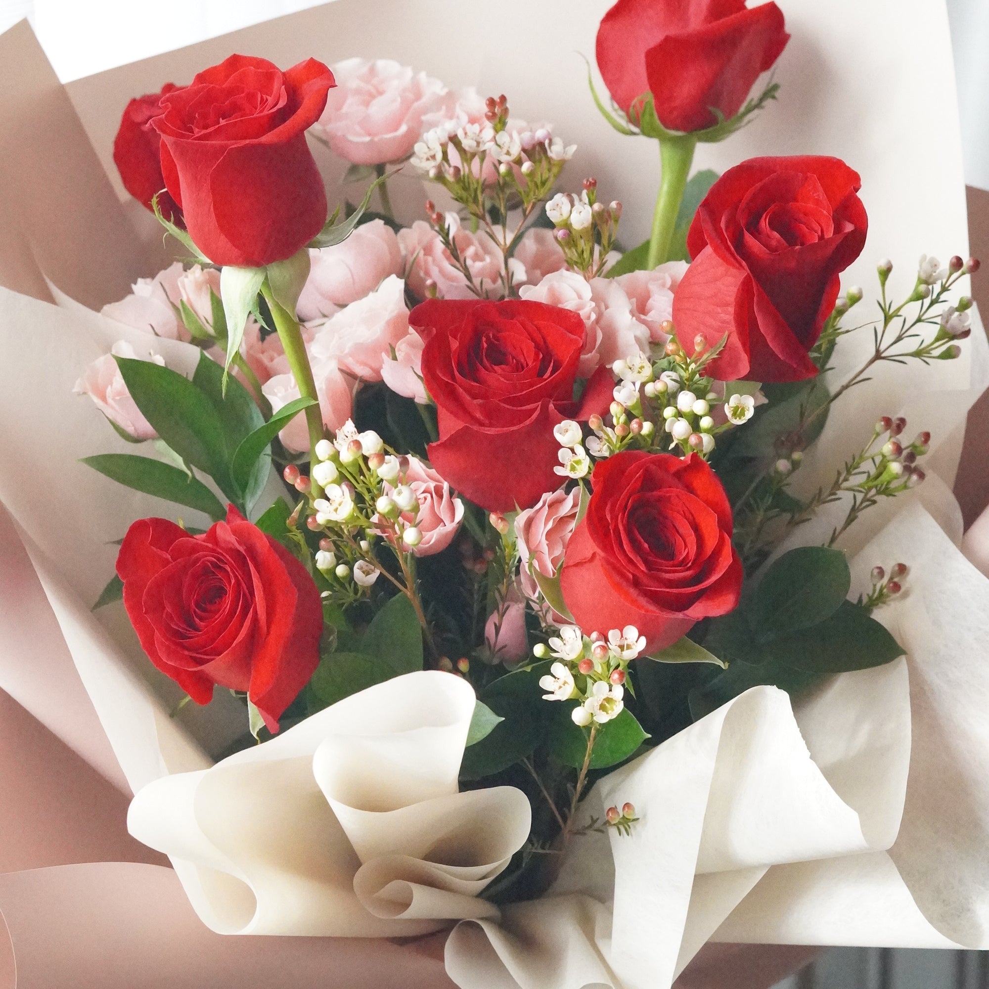 Close-up of red roses and pink spray roses with waxflower highlighting soft color contrast