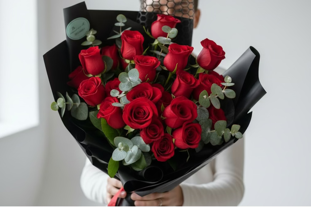 Person holding a classic red rose two dozen bouquet with greenery