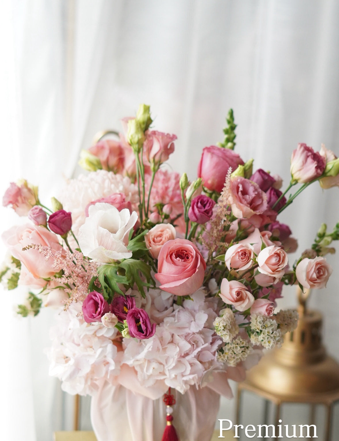 Bouquet of pink and white flowers in a vase with a decorative tassel on a white background.