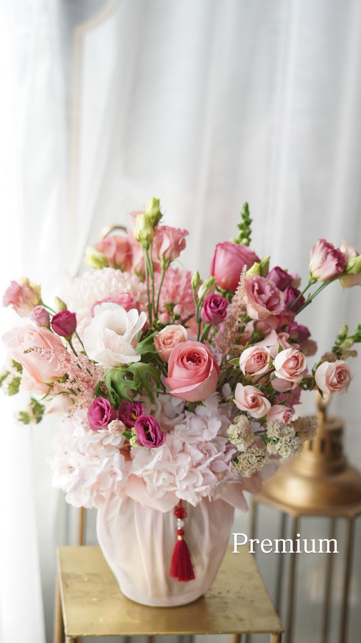 Bouquet of pink and white flowers in a vase with a decorative tassel on a white background.