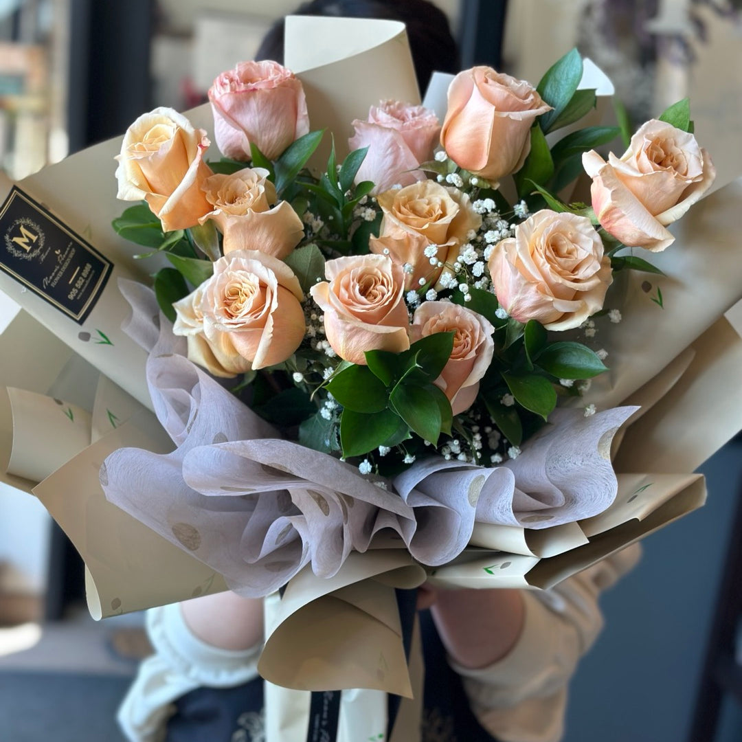 Person holding a classic peach shimmer rose bouquet with greenery