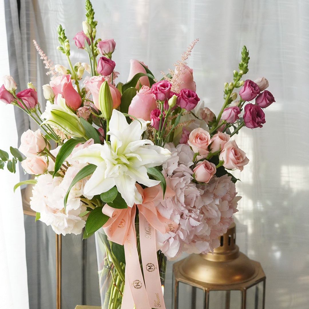 This image showcase the Mix Sympathy Flowers Vase in its Deluxe version. White flowers in this arrangement include lilies, hydrangeas and spray roses. Pink flowers shown are hydrangeas, spray roses, and other seasonal flowers.