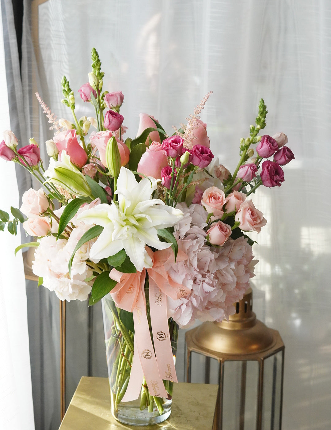 This image showcase the Mix Sympathy Flowers Vase in its Deluxe version. White flowers in this arrangement include lilies, hydrangeas and spray roses. Pink flowers shown are hydrangeas, spray roses, and other seasonal flowers.
