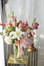 This image showcase the Mix Sympathy Flowers Vase in its Deluxe version. White flowers in this arrangement include lilies, hydrangeas and spray roses. Pink flowers shown are hydrangeas, spray roses, and other seasonal flowers.