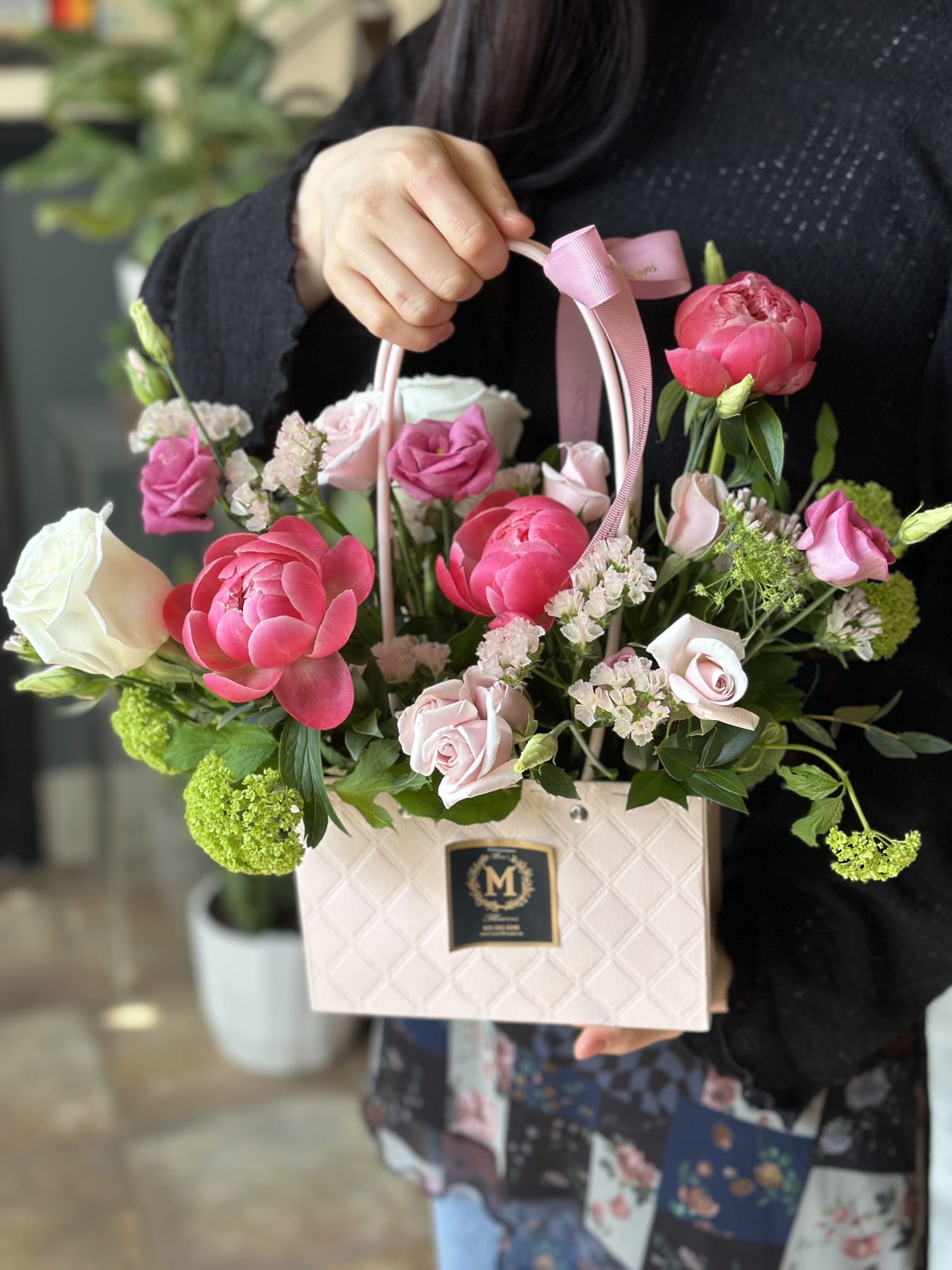 A beautiful Mother's Day flower basket featuring fresh coral peonies, spray roses, lisianthus, and mixed greenery. Hand-tied bouquet arrangement with a pink ribbon, available for same-day delivery in Toronto by Moon's Flowers