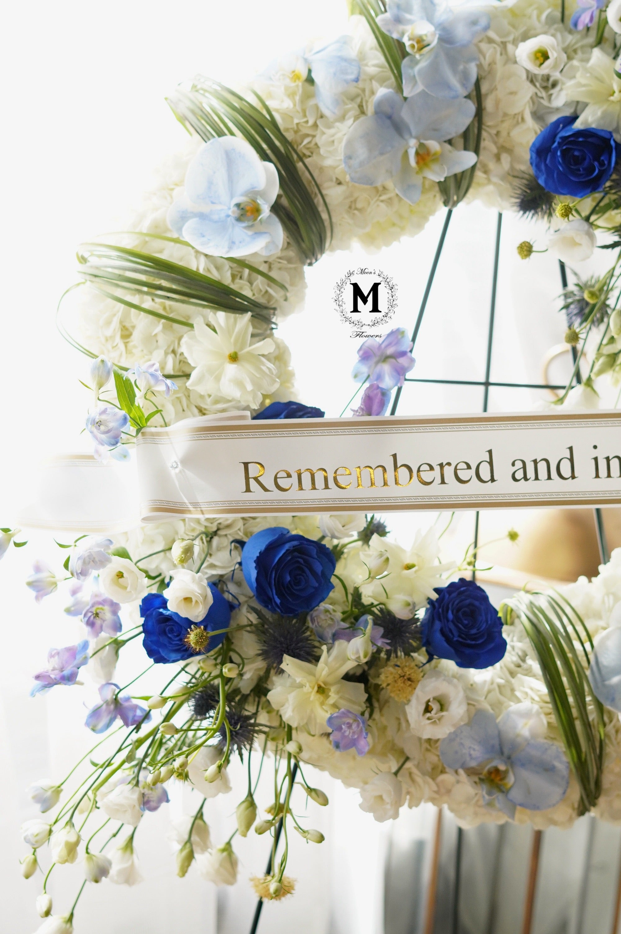 Personalized funeral tribute with blue flowers and custom printed sympathy ribbon by Moon's Flowers