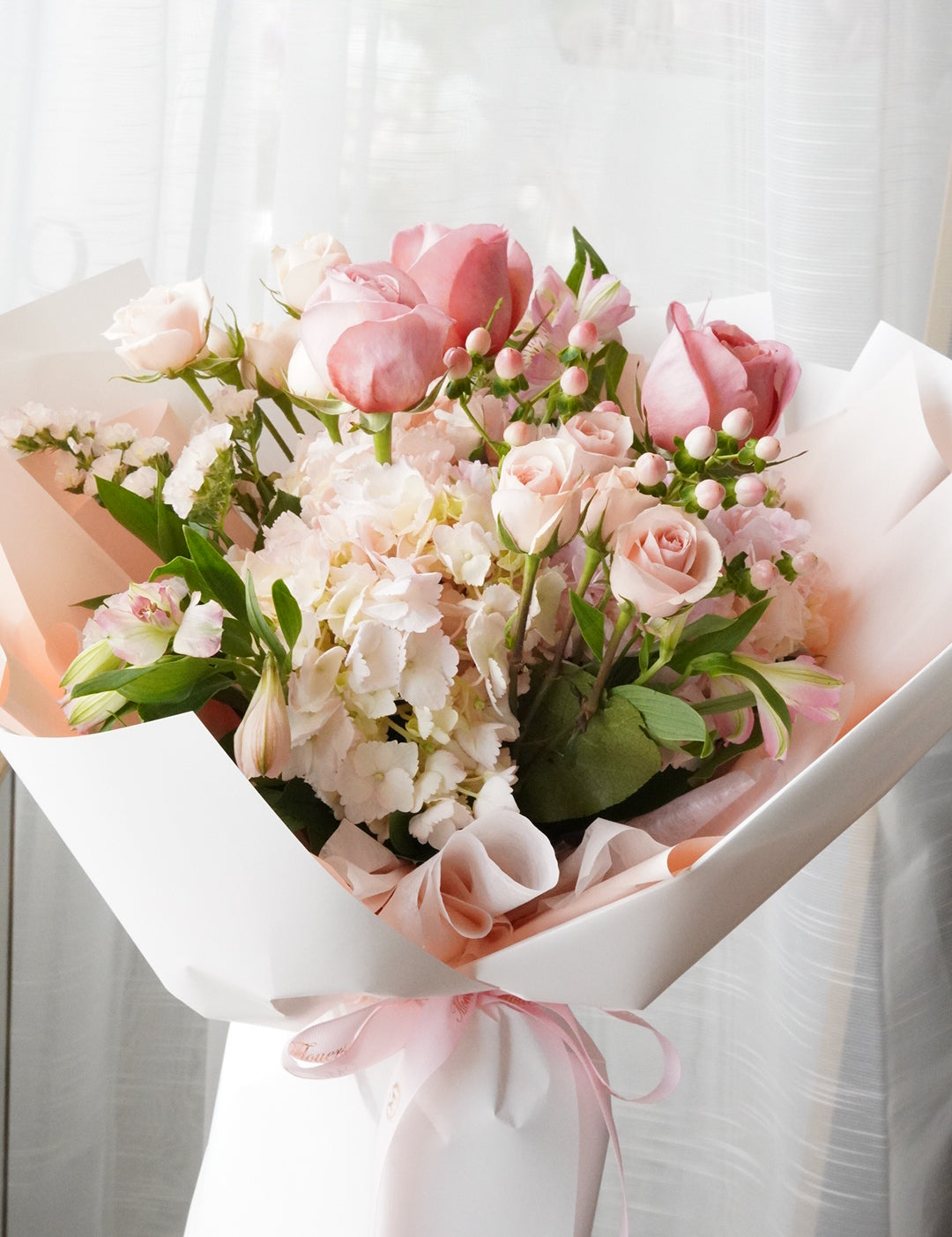 Bouquet of pink and white flowers wrapped in paper on a light background