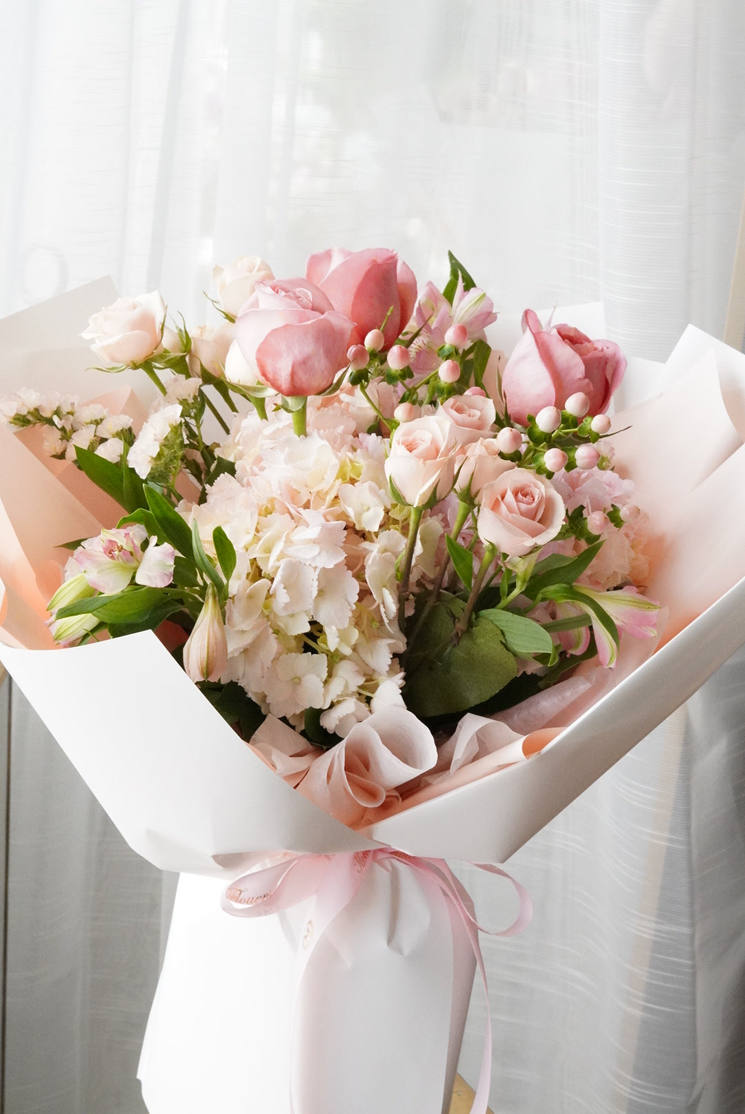 Bouquet of pink and white flowers wrapped in paper on a light background