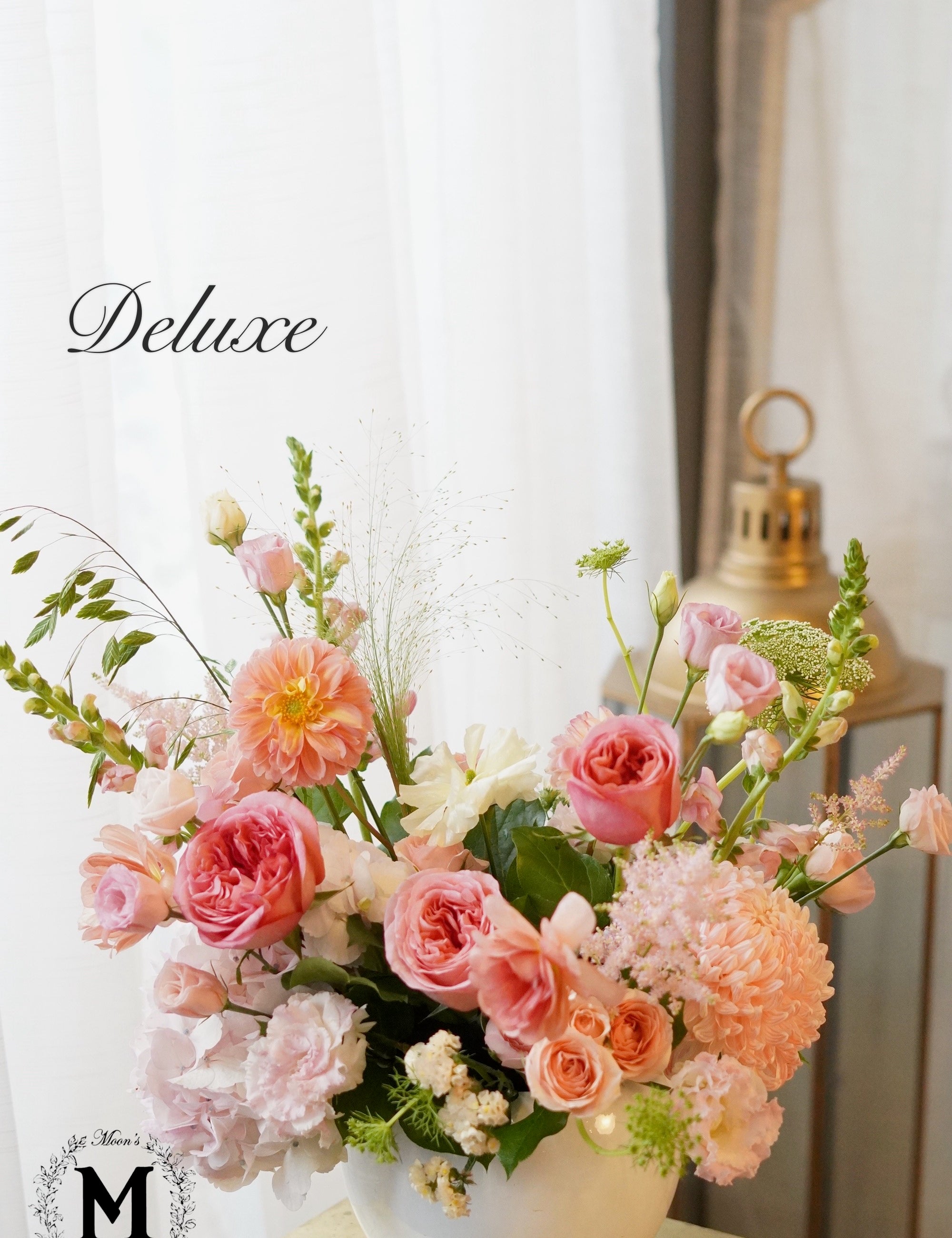 Deluxe flower arrangement in a white vase with soft pink and green tones on a light background.