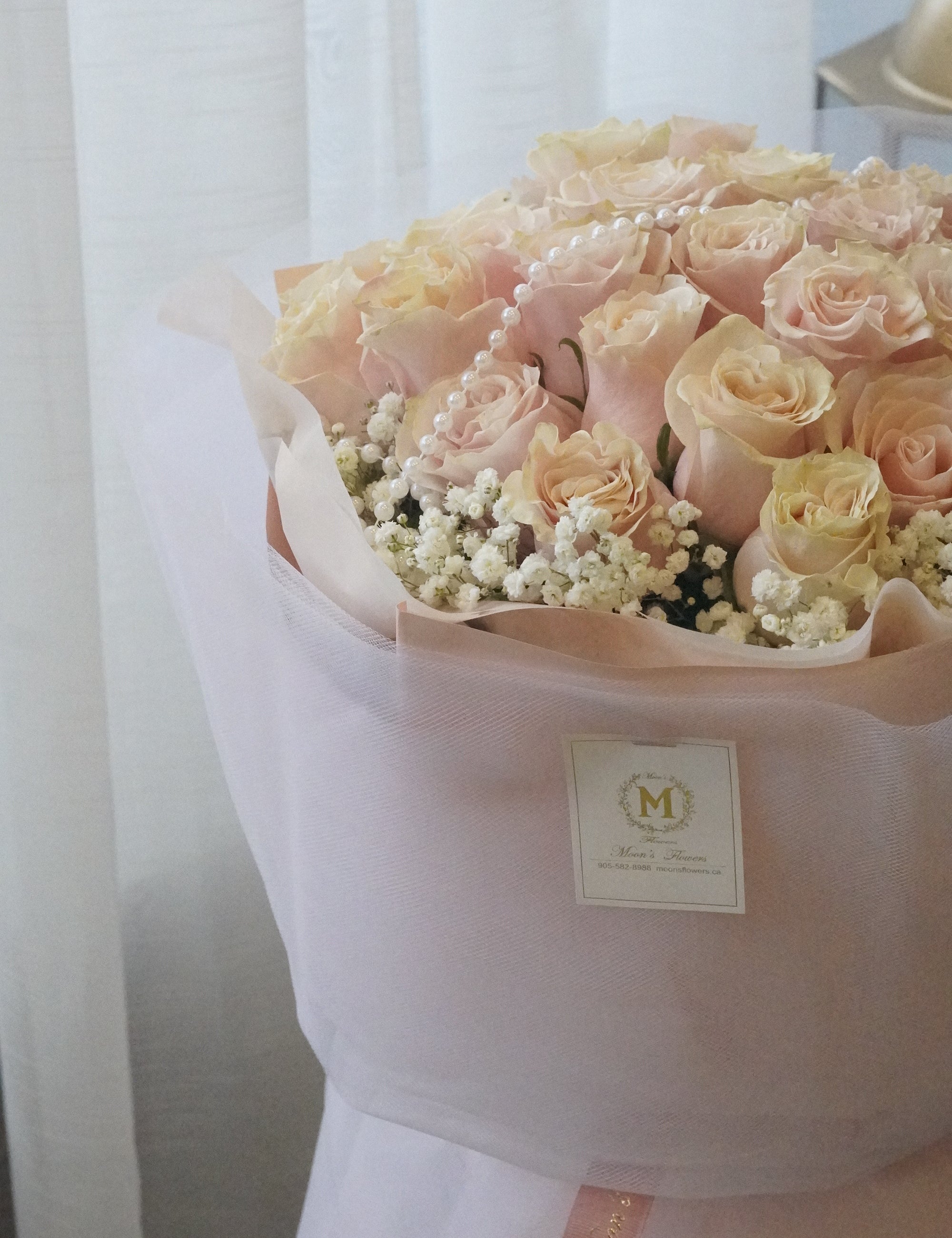 Bouquet of pink and white flowers wrapped in white paper with a Moon's Flowers brand label.