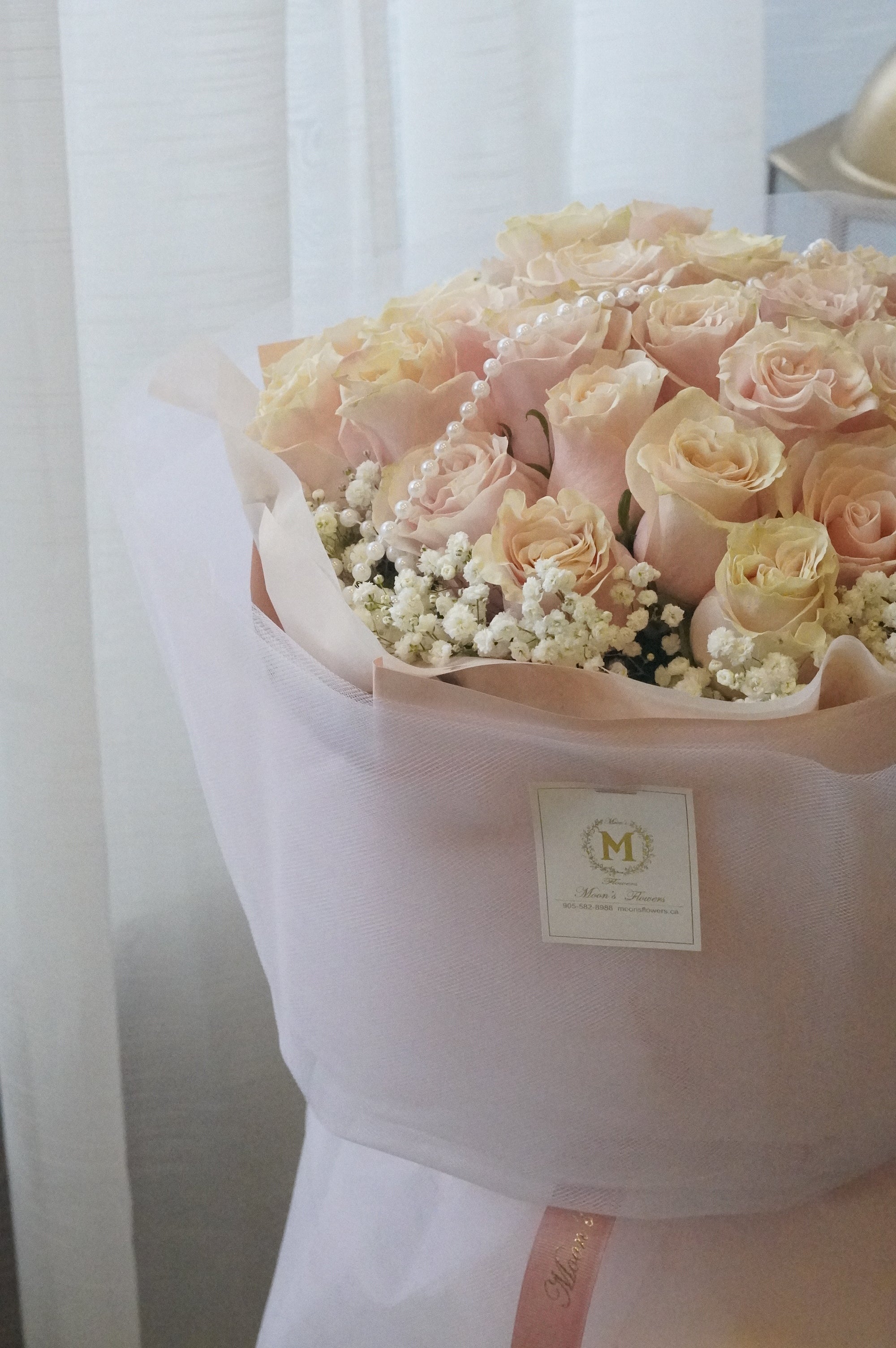 Bouquet of pink and white flowers wrapped in white paper with a Moon's Flowers brand label.