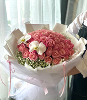 Bouquet of pink roses and white orchids wrapped in white paper with a ribbon, perfect for engagements for grand gestures of love