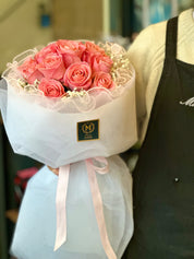 Bouquet of pink roses wrapped in white paper with a visible brand logo.