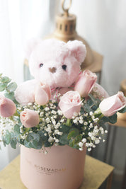 Pink rose arrangement in hat box with teddy bear and eucalyptus greenery
