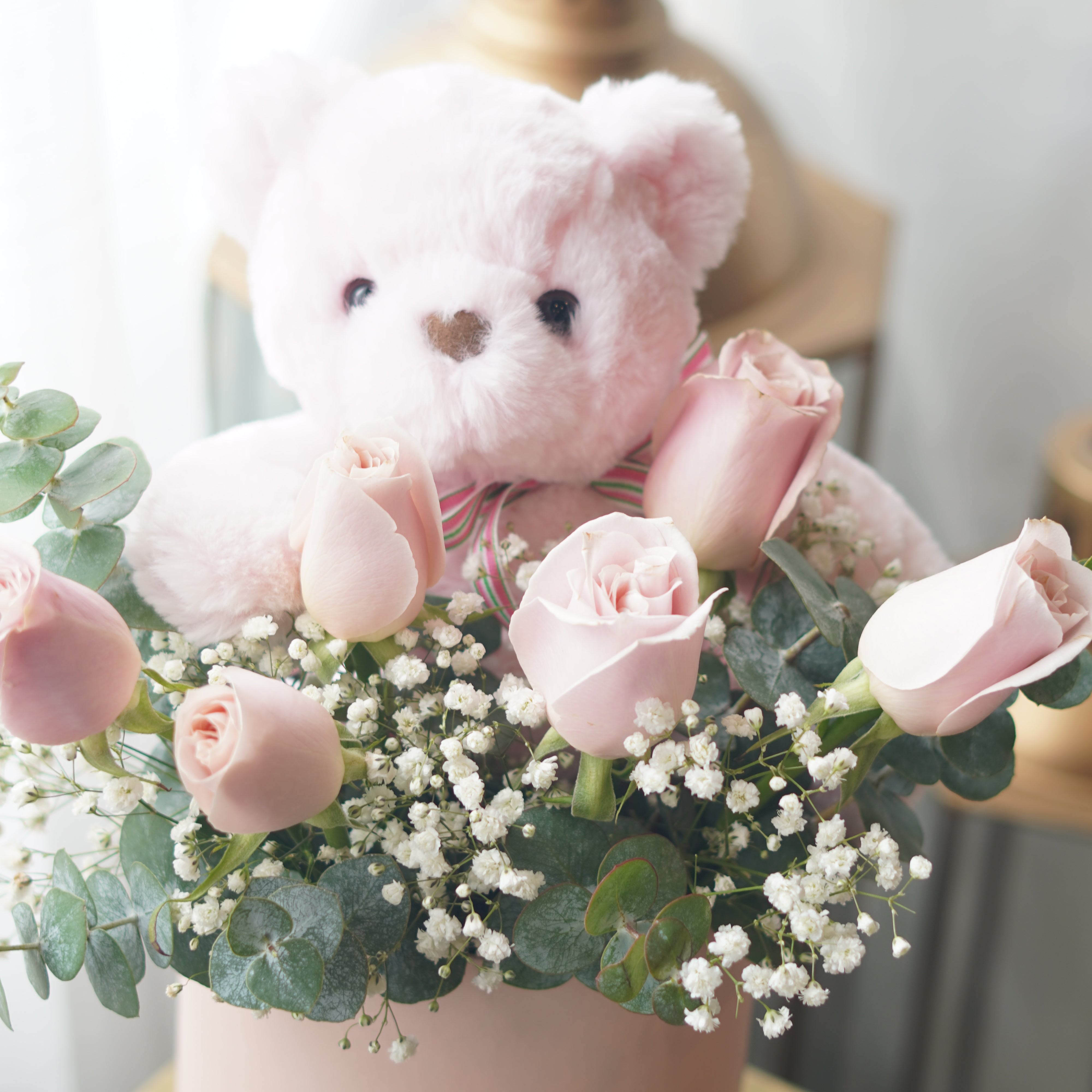 Pink rose arrangement in hat box with teddy bear and eucalyptus greenery
