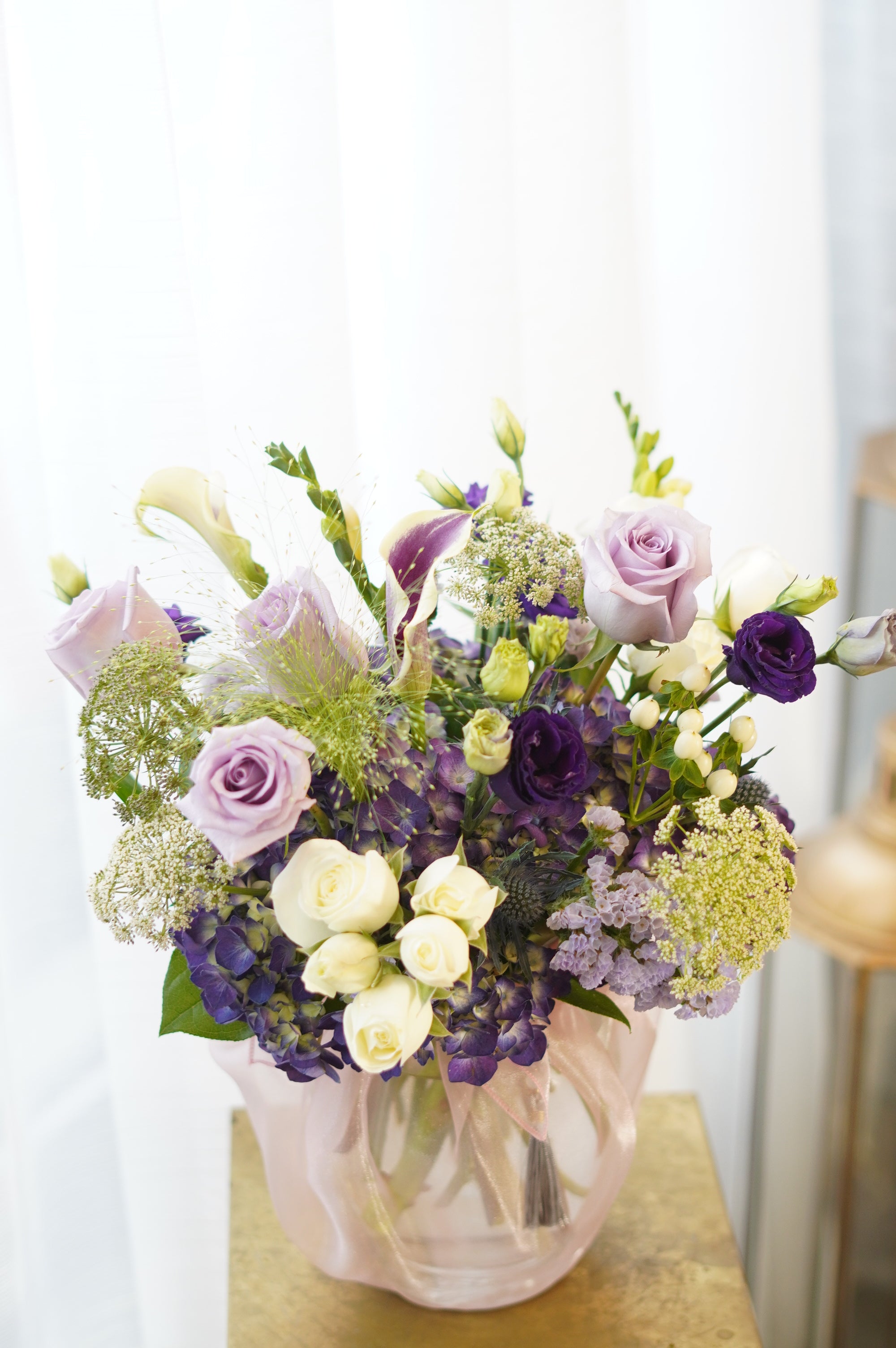 Purple and lavender Mother's Day floral arrangement featuring premium roses, dark purple lisianthus, and white calla lilies in a fabric-wrapped vase with a traditional Korean tassel. Professional flower delivery in Toronto and Oakville.