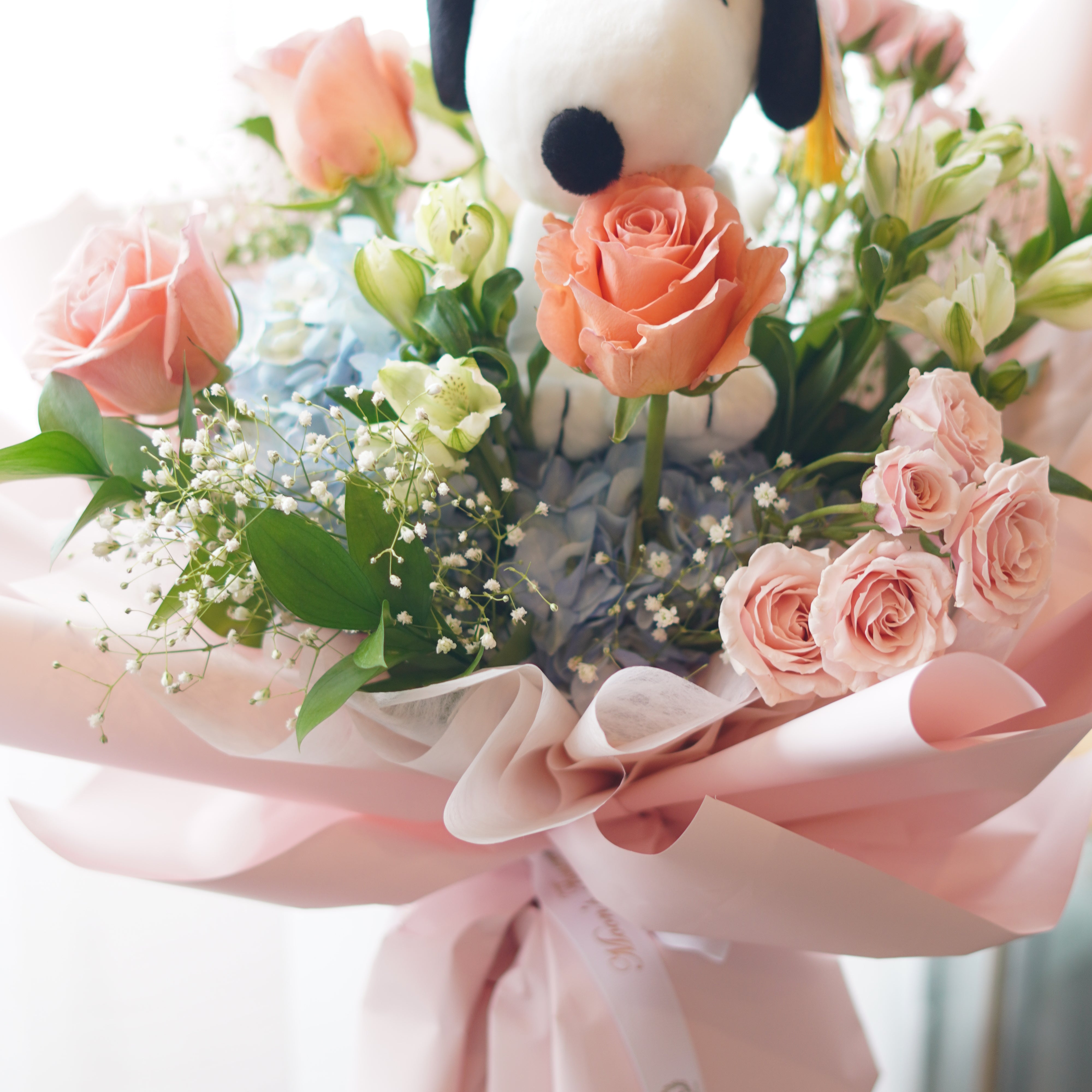 Snoopy graduation bouquet full view with pastel flowers, blue hydrangea, peach roses, and pink wrapping
