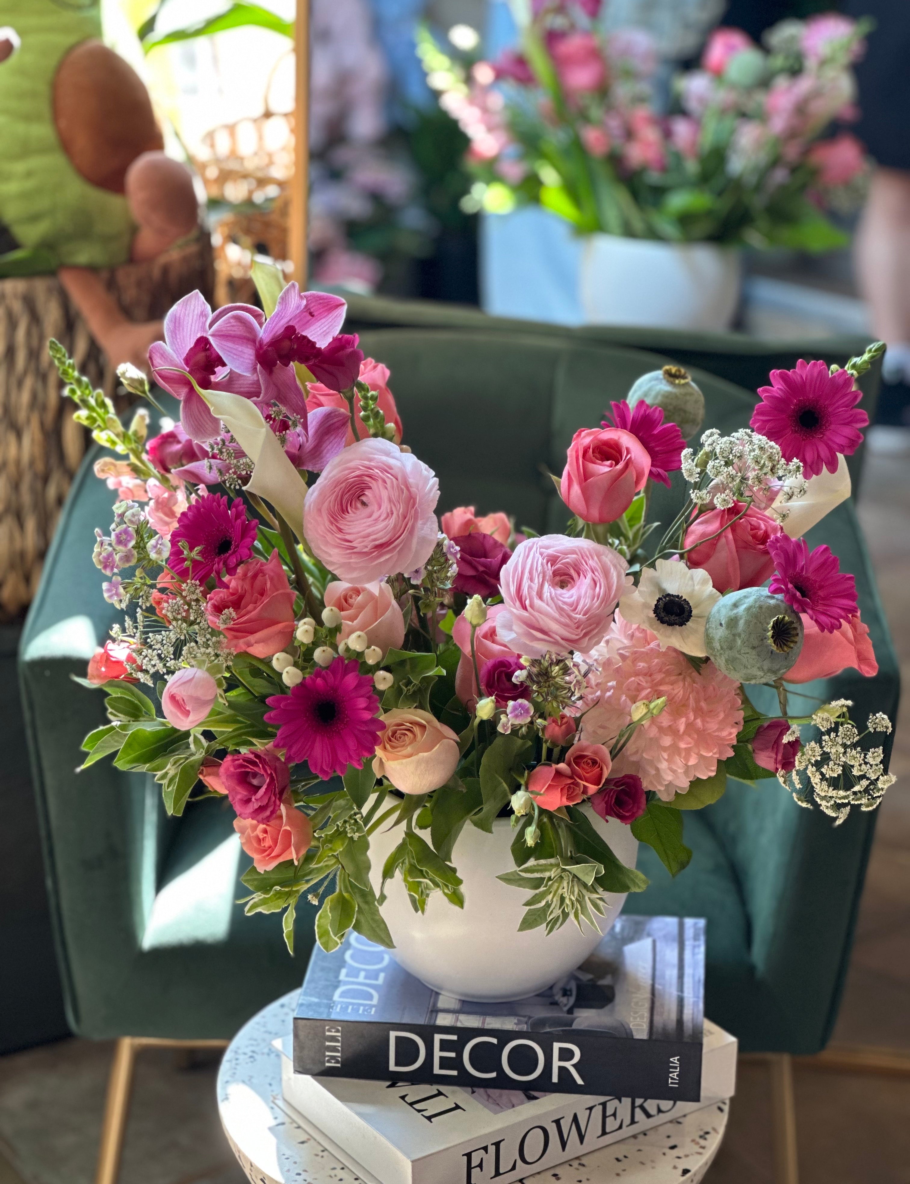A floral arrangement featuring pink, purple, and white flowers in a white vase, placed on a surface with a book titled 'Decor'.