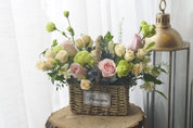 Pink rose and mixed greenery flower arrangement in a handwoven straw basket