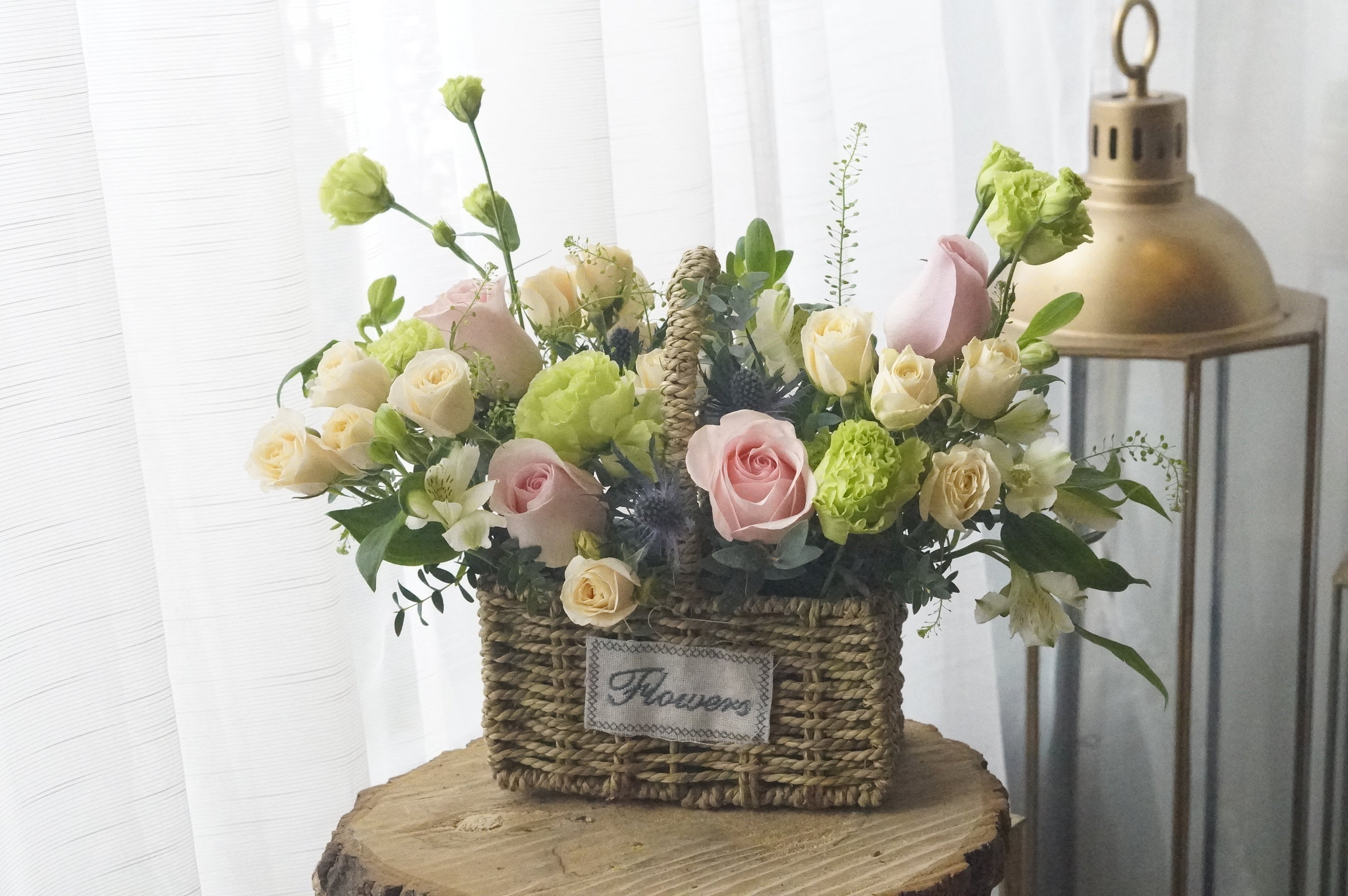 Pink rose and mixed greenery flower arrangement in a handwoven straw basket