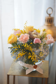 Spring pastel flower arrangement with hydrangeas, roses, mimosa, and decorative nest in glass bowl