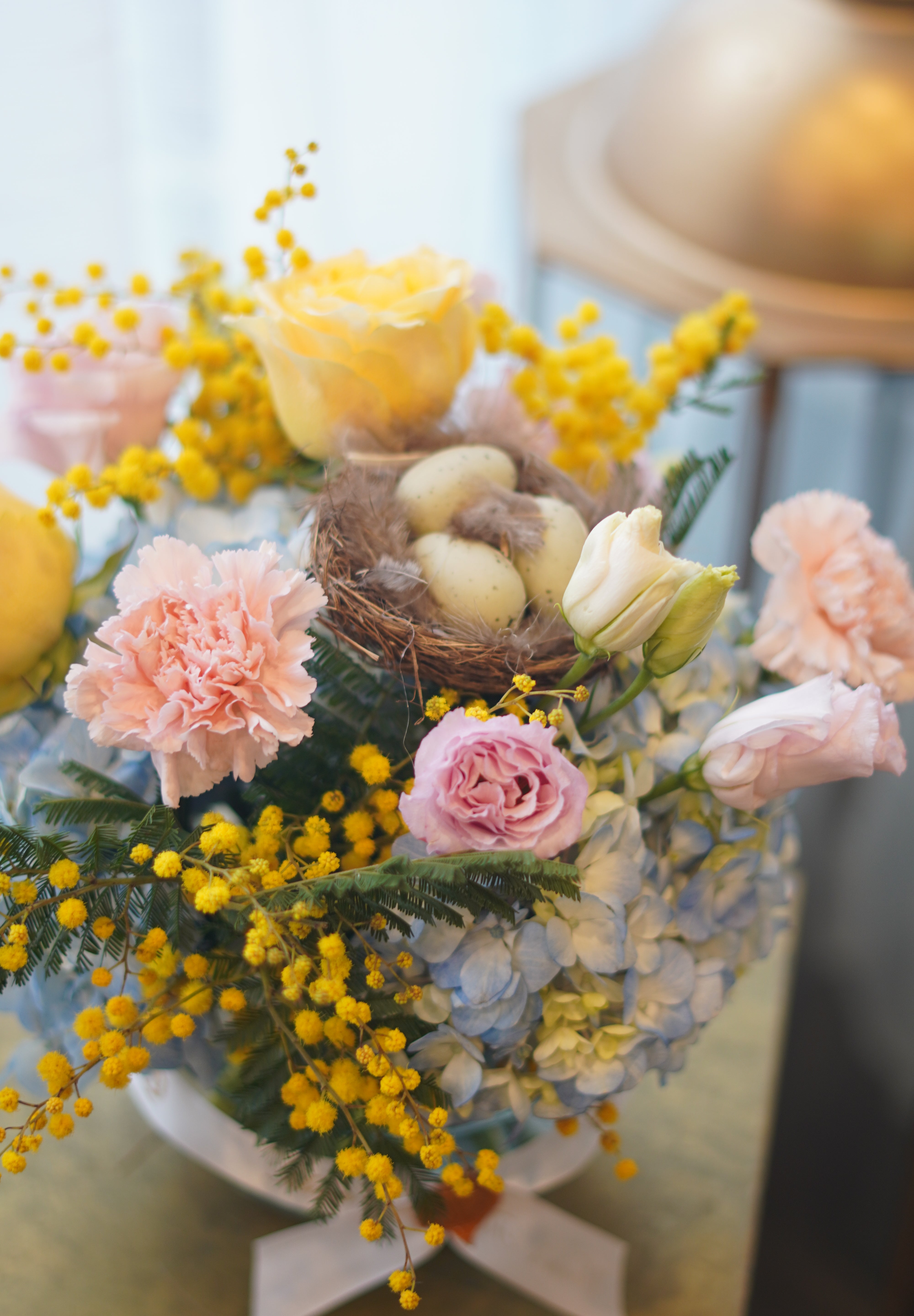 Spring pastel flower arrangement with hydrangeas, roses, mimosa, and decorative nest in glass bowl