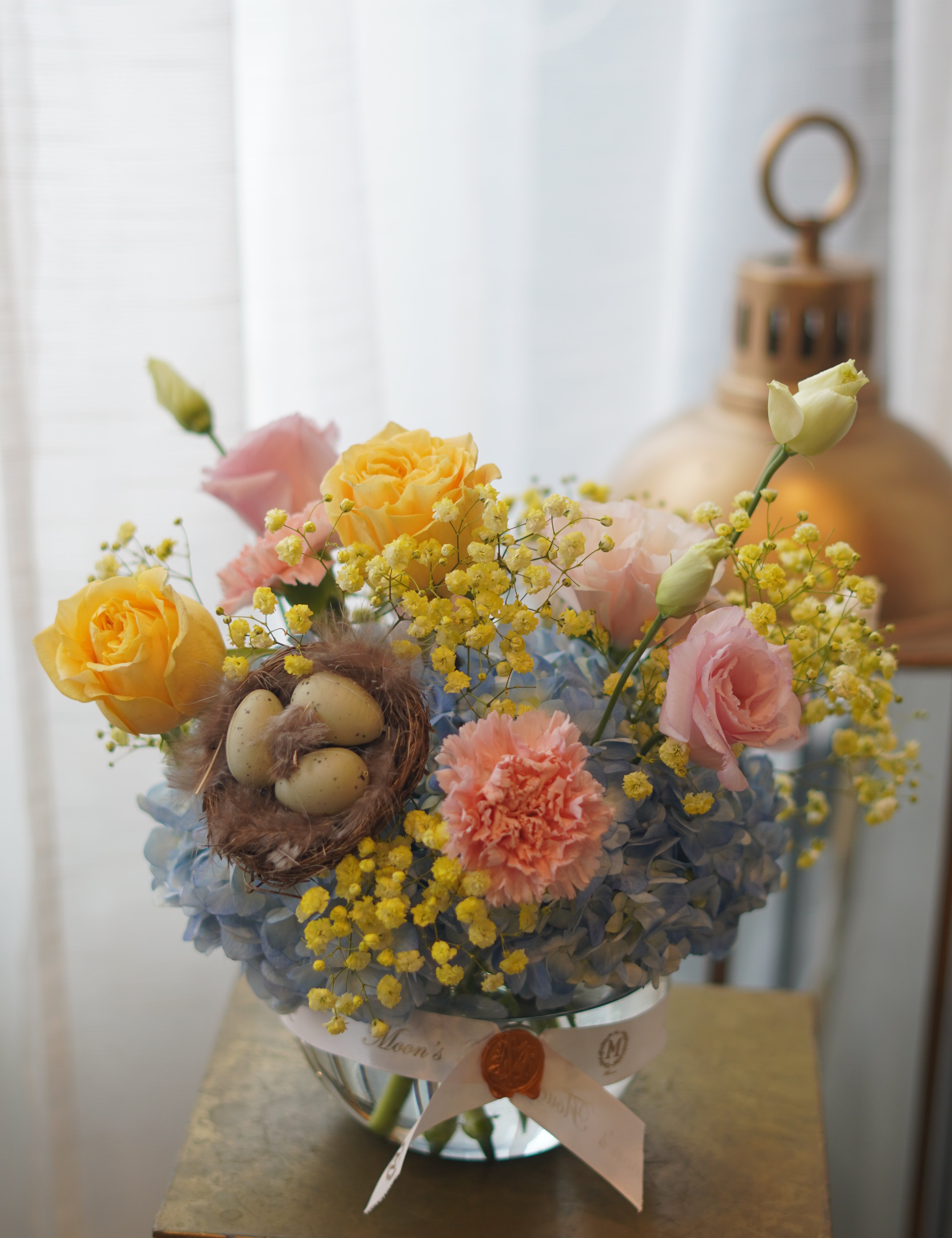 Spring pastel flower arrangement with hydrangeas, roses, mimosa, and decorative nest in glass bowl