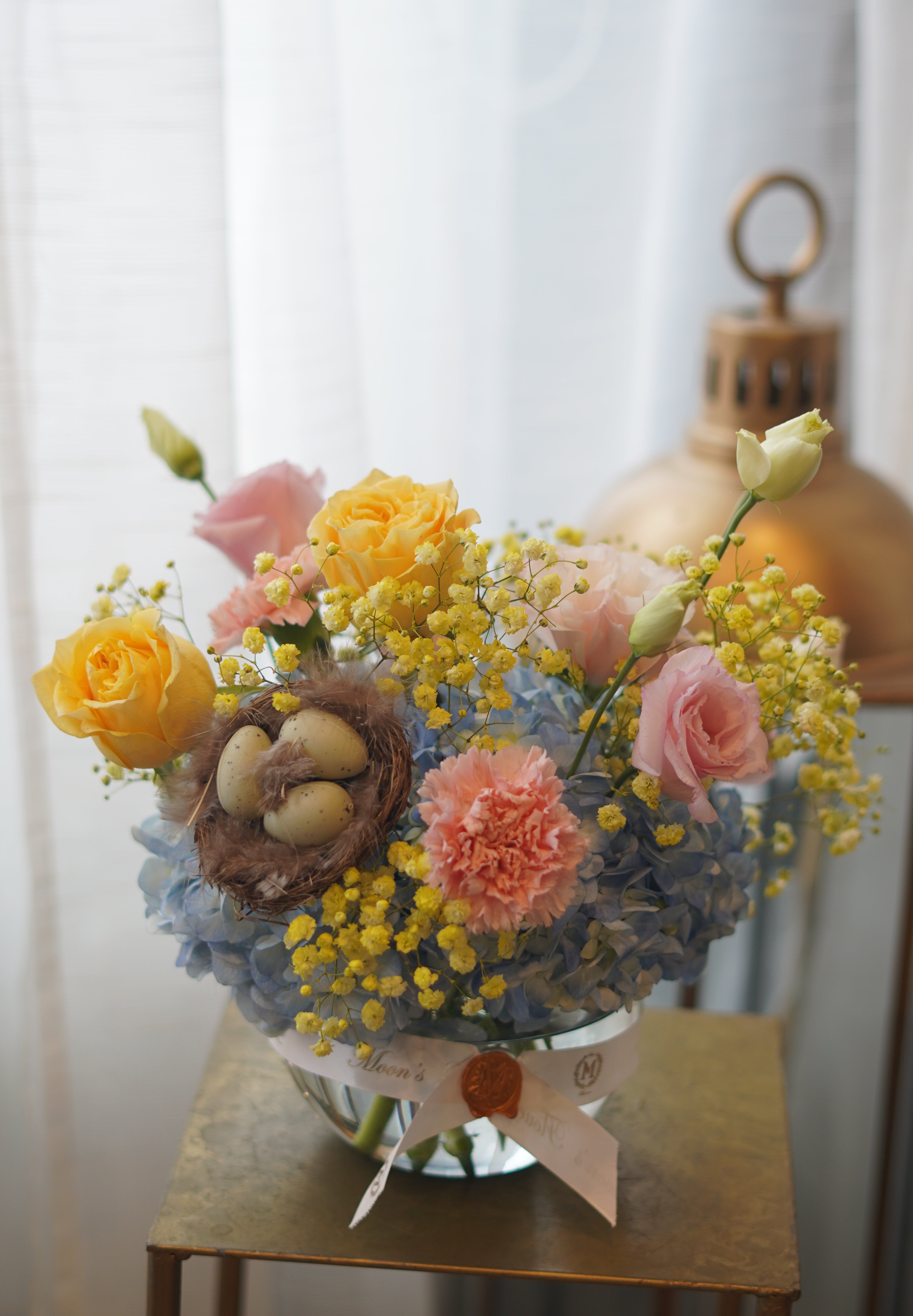 Spring pastel flower arrangement with hydrangeas, roses, mimosa, and decorative nest in glass bowl