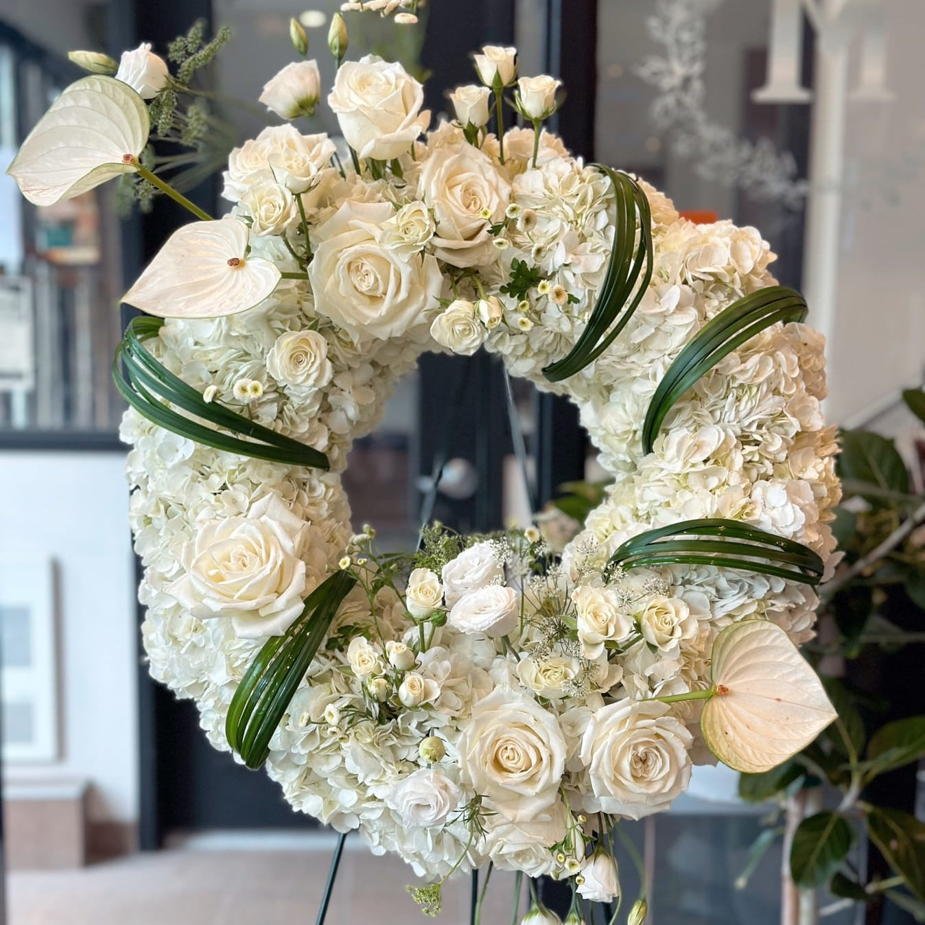 Standing  funeral wreath with white roses, hydrangeas, and lilies on a florist easel for same-day delivery in Toronto