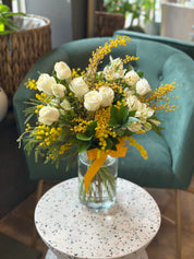 A floral arrangement with white roses and yellow flowers, placed in a clear vase, set against a home decor background.