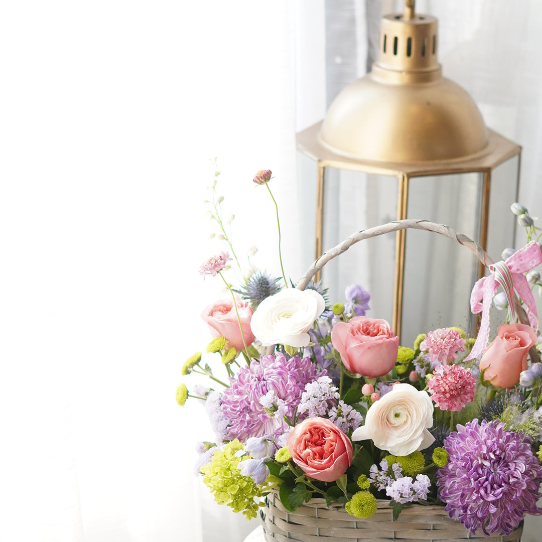 elegant spring flower basket with pink roses, purple blooms and greenery near window