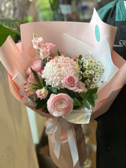 A bouquet of flowers with pink and white colors, wrapped in pale pink paper with a decorative ribbon.