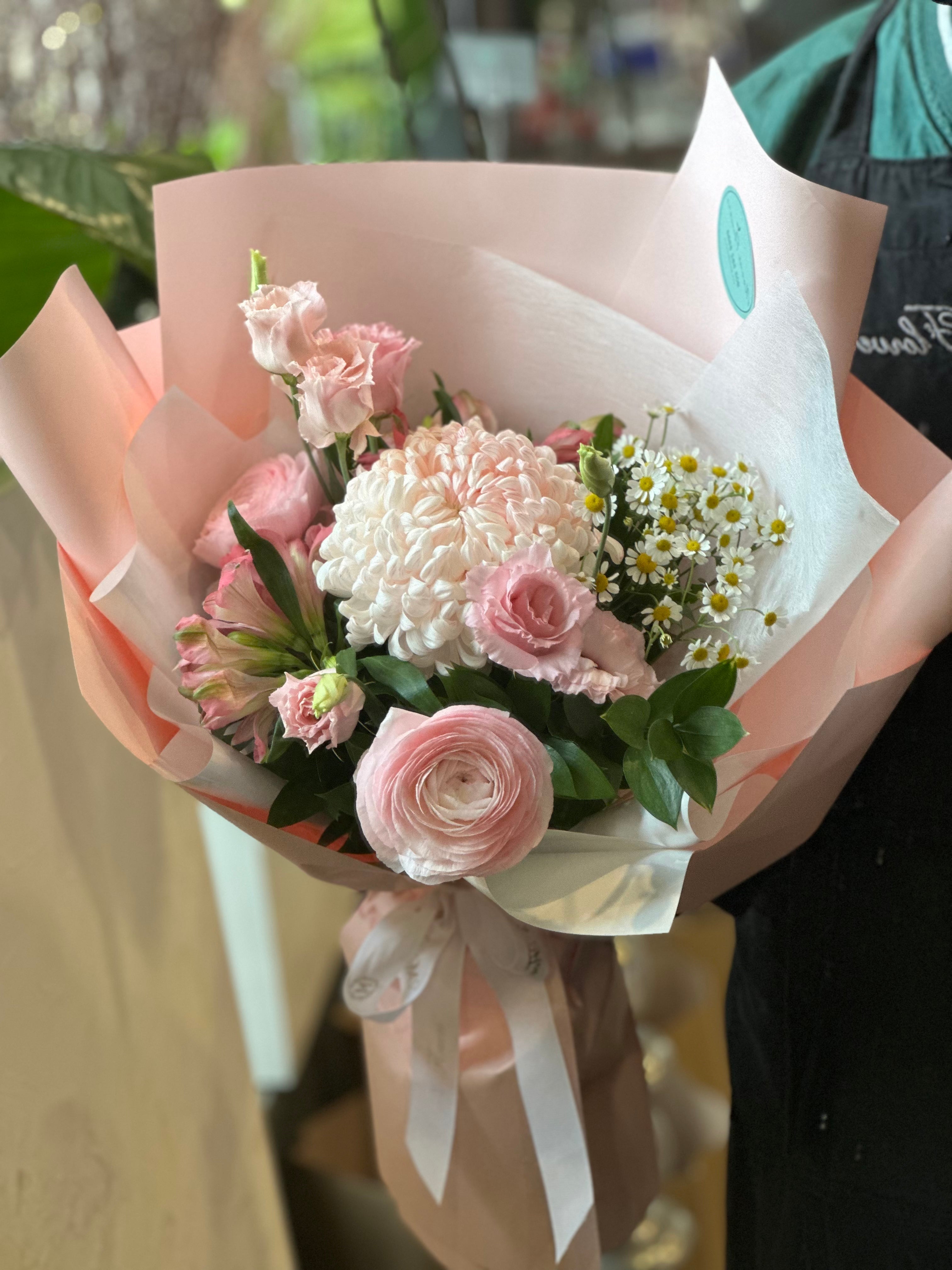 A bouquet of flowers with pink and white colors, wrapped in pale pink paper with a decorative ribbon.
