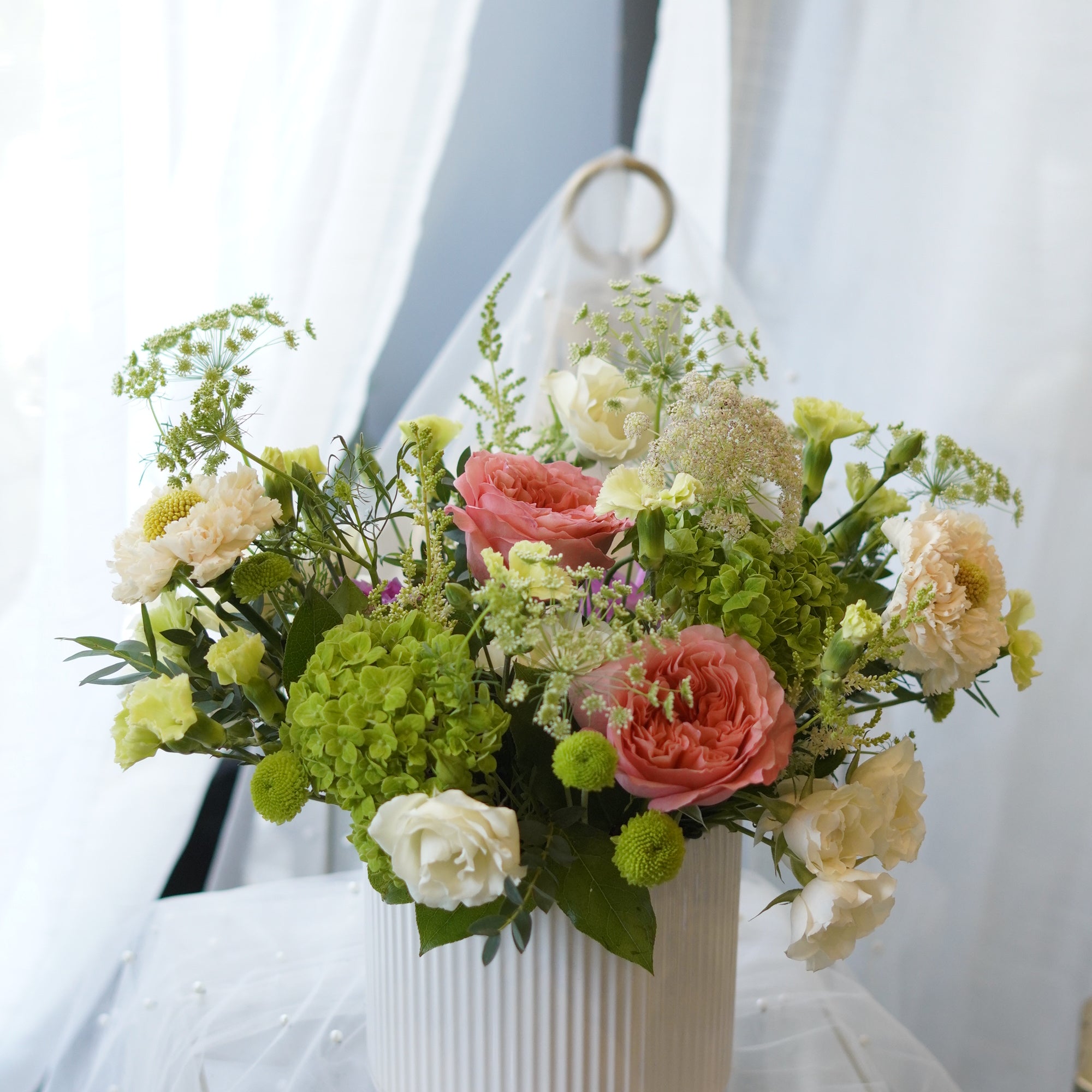 Sunday Brunch garden-style centerpiece with coral roses, green hydrangeas, and seasonal flowers in a white ceramic vase by Moon's Flowers Oakville.