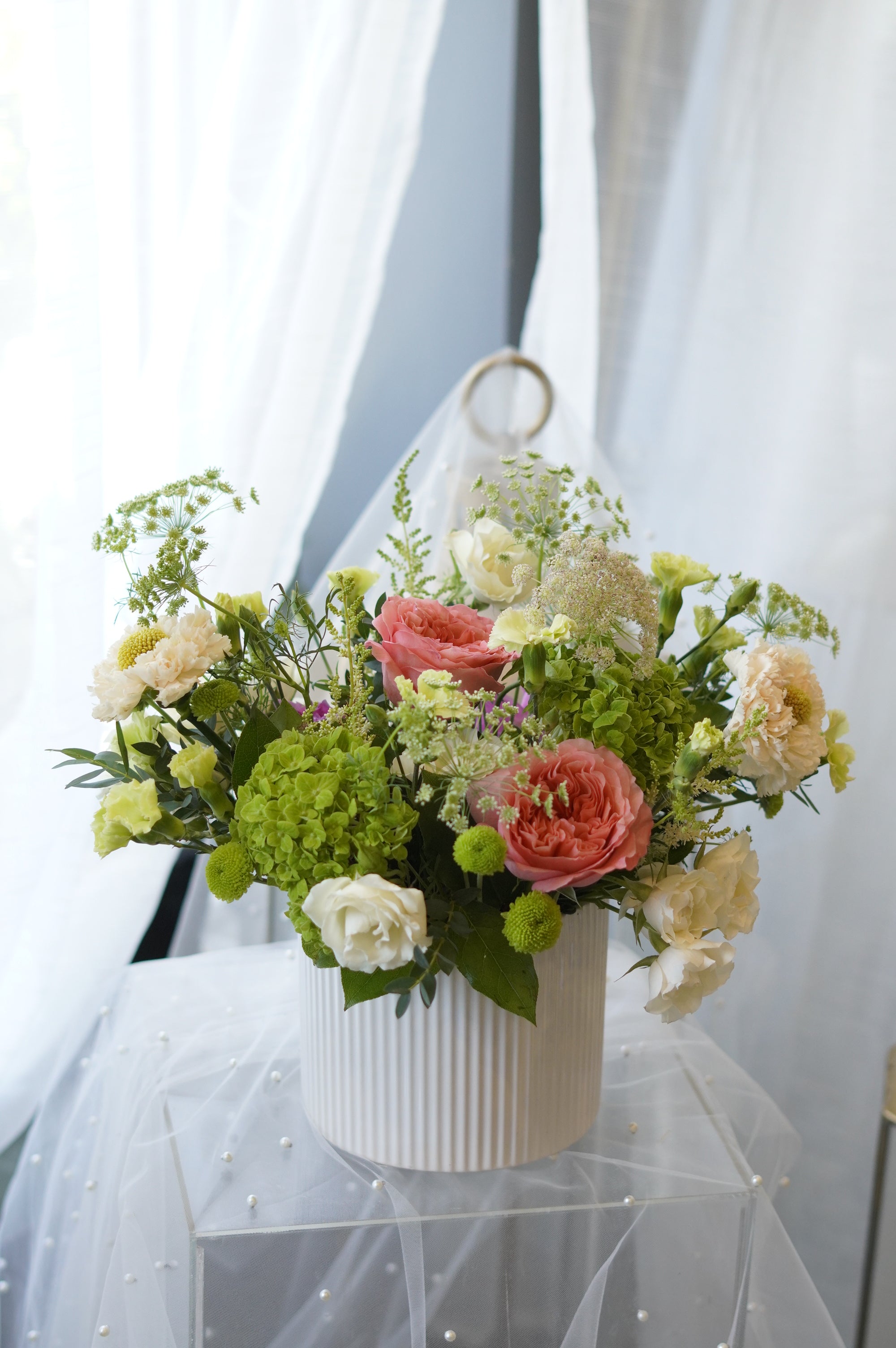 Sunday Brunch garden-style centerpiece with coral roses, green hydrangeas, and seasonal flowers in a white ceramic vase by Moon's Flowers Oakville.