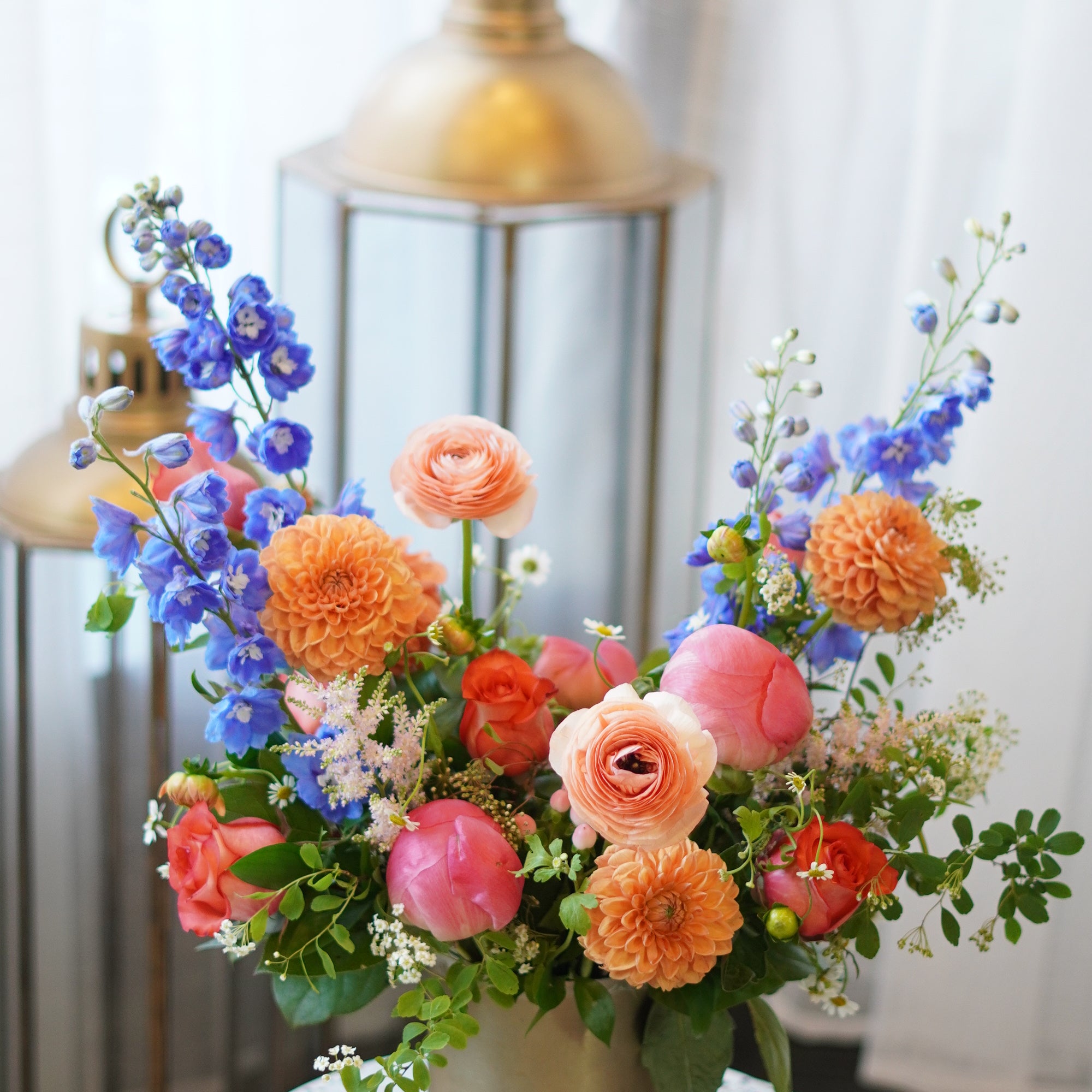 Sunset Serenity flower arrangement with orange dahlias, coral peonies, and blue delphiniums in a gold vase. Luxury Mother's Day floral gift for same-day delivery in Toronto by Moon's Flowers.