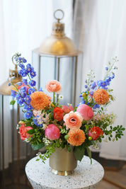 Sunset Serenity flower arrangement with orange dahlias, coral peonies, and blue delphiniums in a gold vase. Luxury Mother's Day floral gift for same-day delivery in Toronto by Moon's Flowers.