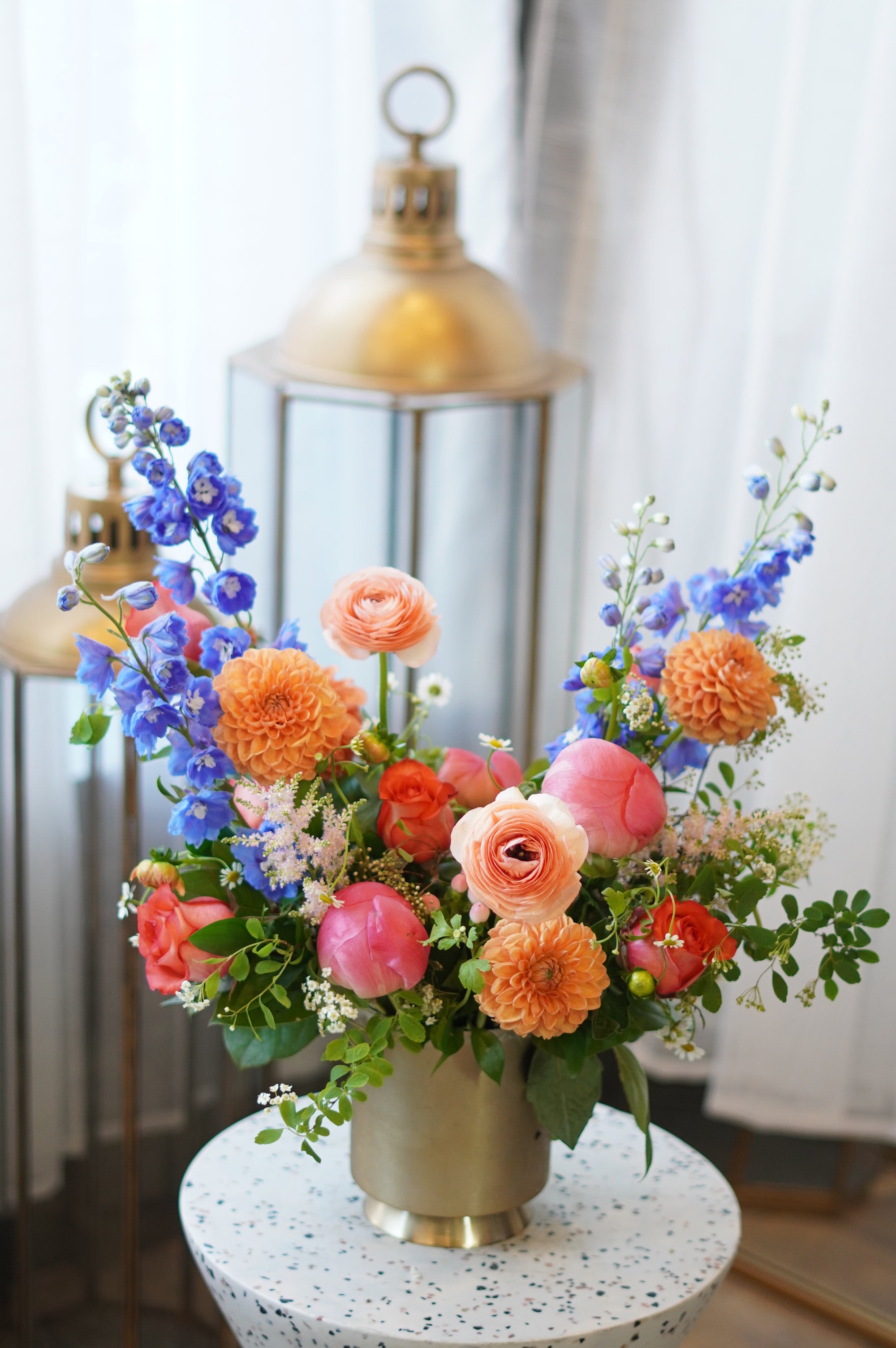 Sunset Serenity flower arrangement with orange dahlias, coral peonies, and blue delphiniums in a gold vase. Luxury Mother's Day floral gift for same-day delivery in Toronto by Moon's Flowers.