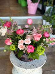 Top-down view of the 'Flowers in a Basket' featuring a lush mix of pink roses, bright peonies, and green hydrangeas on a white speckled stool. A charming Mother's Day floral arrangement by Moon's Flowers Toronto