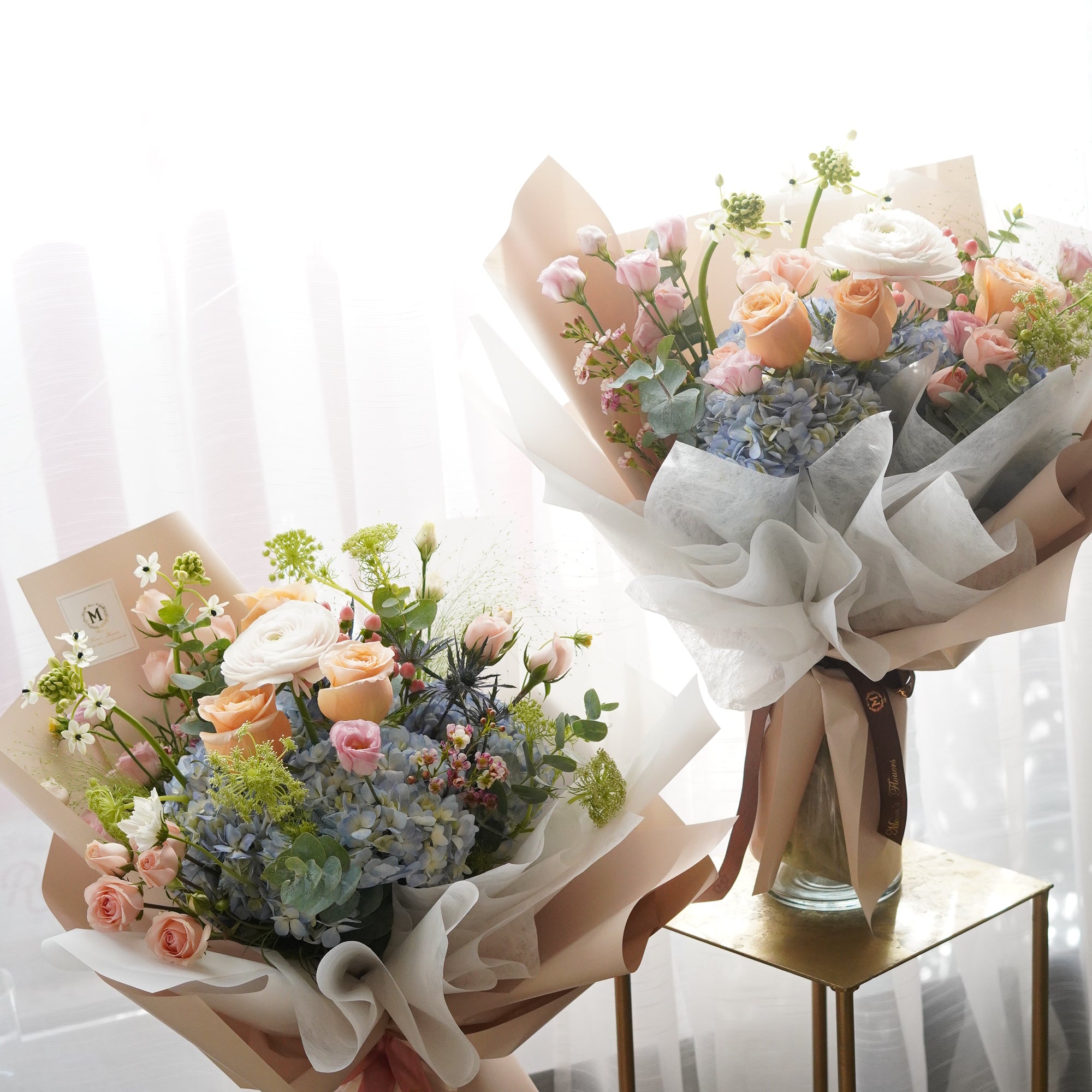 Two elegant Mother's Day 'Golden Hour' bouquets side by side, featuring peach roses and purple hydrangeas in designer wrapping. Professional hand-tied floral arrangements by Moon's Flowers Toronto, perfect for gifting