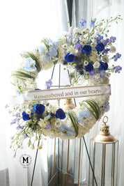 Personalized funeral tribute with blue flowers and custom printed sympathy ribbon by Moon's Flowers.