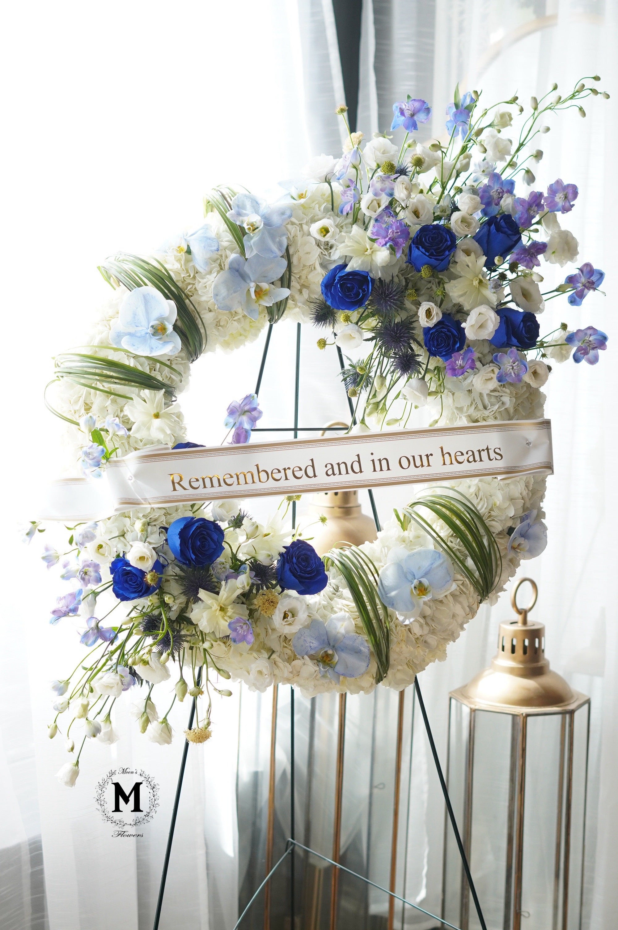 Personalized funeral tribute with blue flowers and custom printed sympathy ribbon by Moon's Flowers.