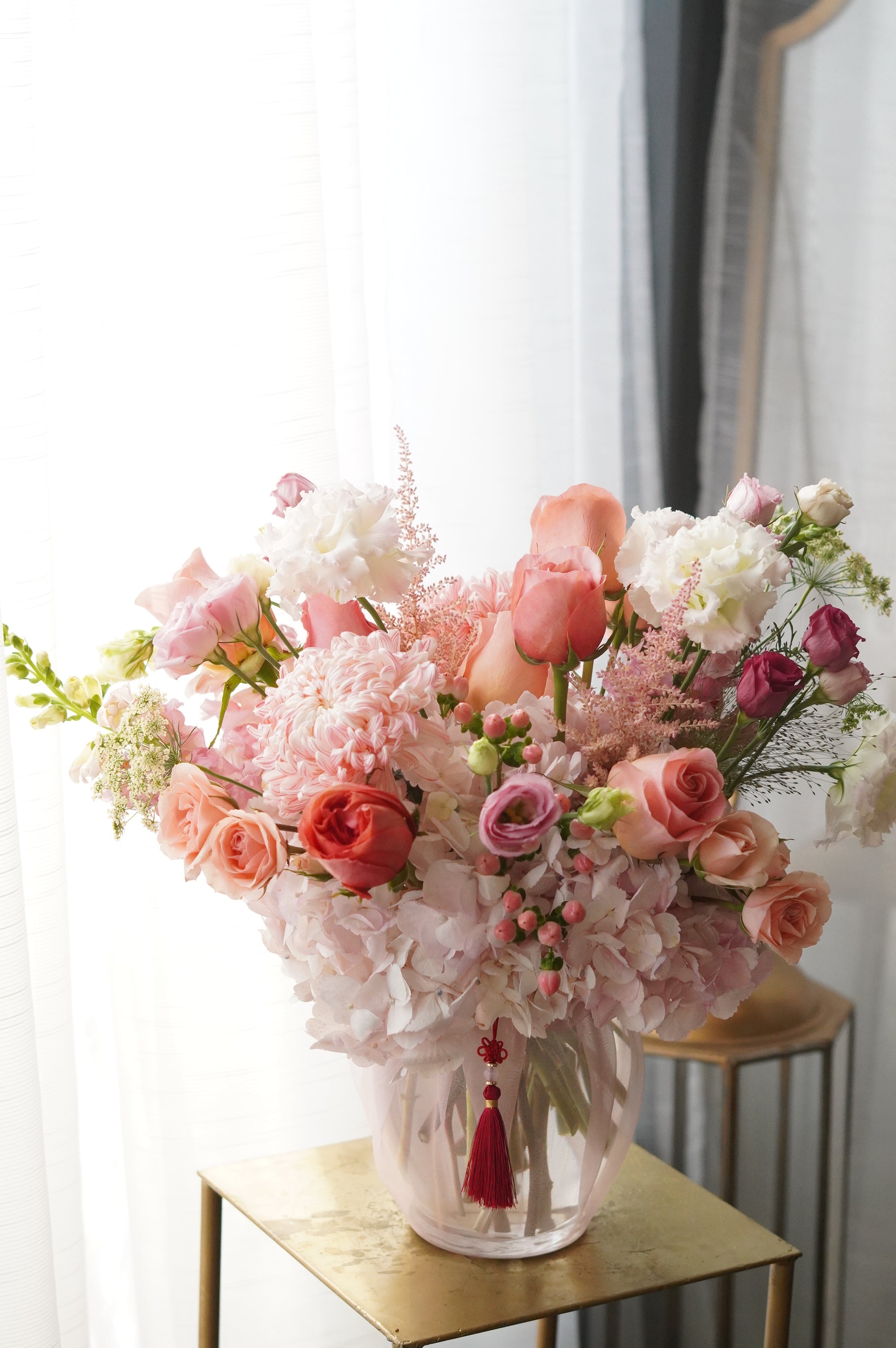 Lush Mother's Day floral arrangement in a glass vase featuring peach roses, pink hydrangeas, and delicate astilbe with a traditional Korean decorative tassel. Premium flower delivery in Toronto and Oakville.