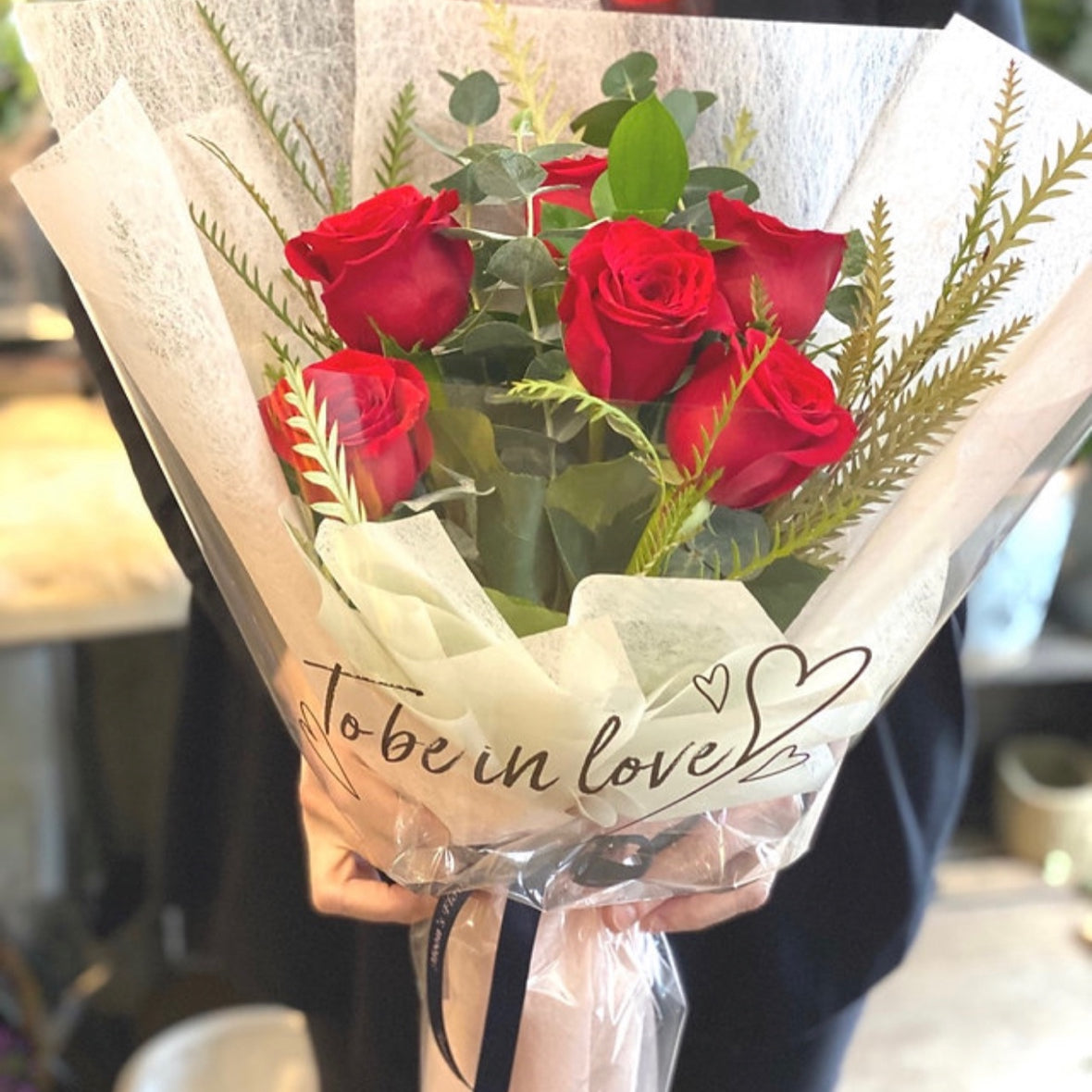 Half dozen rose bouquet held by hand, wrapped in Moon’s Flowers’ signature style